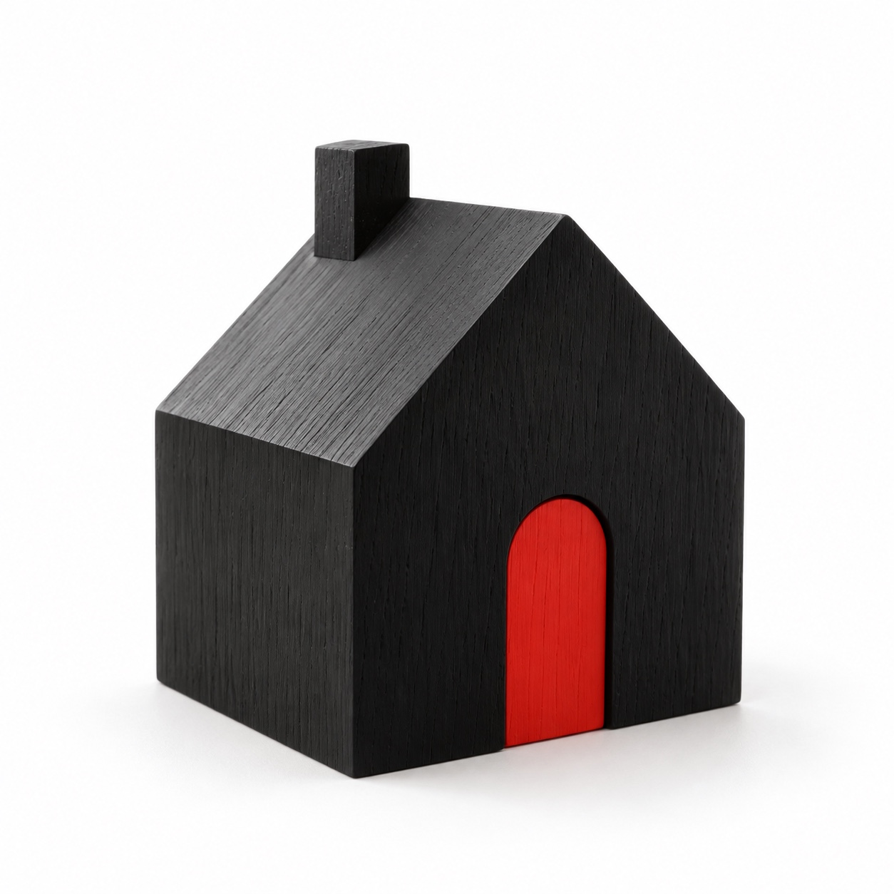 A sculptural black wooden house with a red arched door on a white background